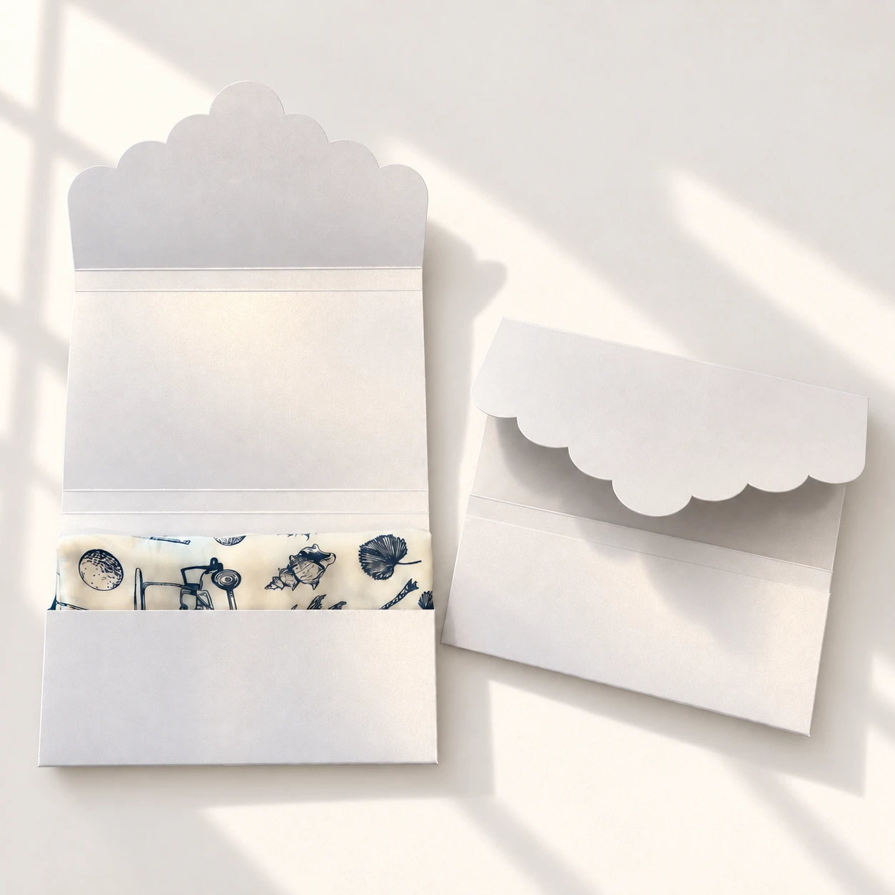 Two blank scalloped display envelopes in soft white — one open revealing a custom illustrated silk scarf, one closed
